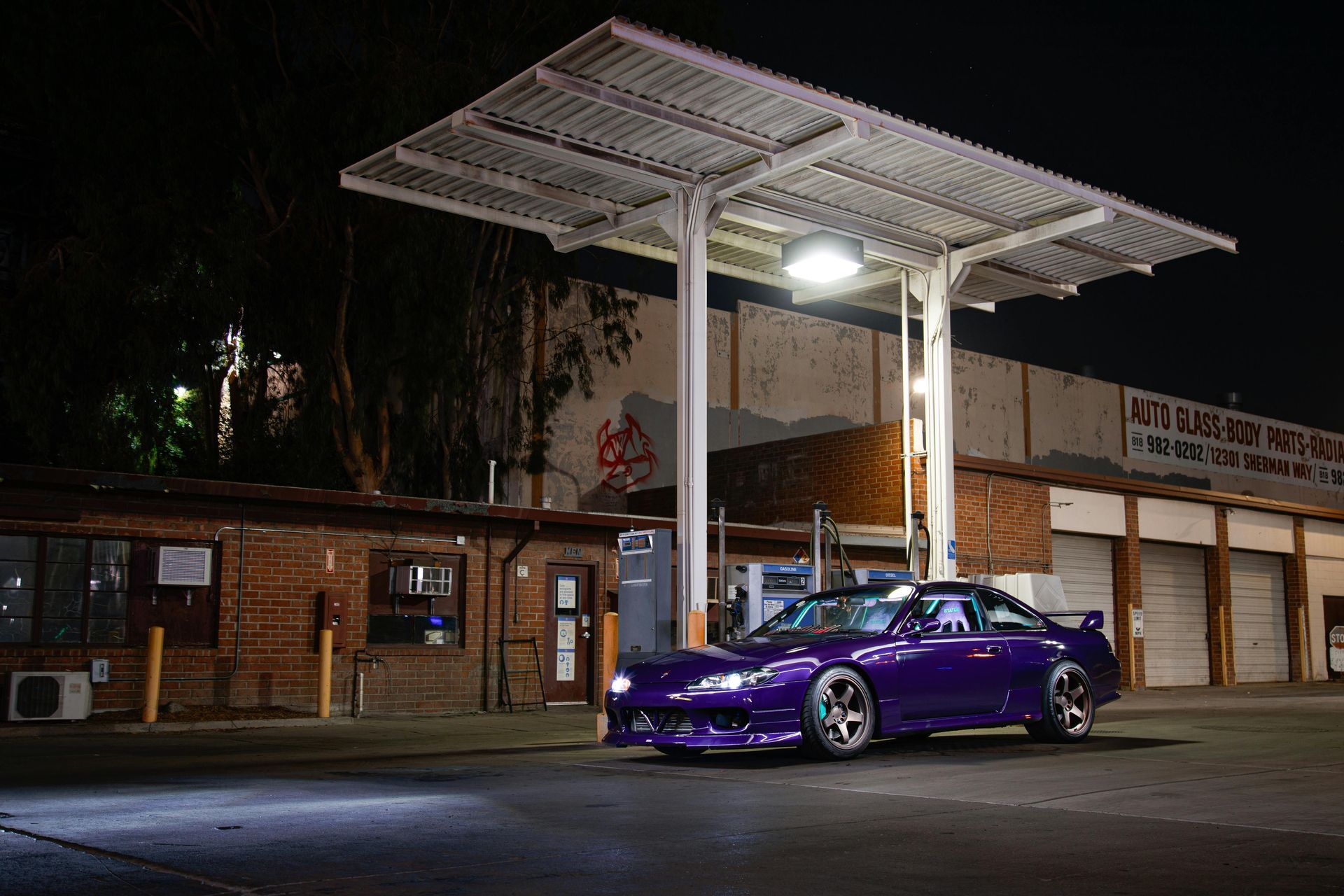 A purple car is parked in front of a gas station at night.