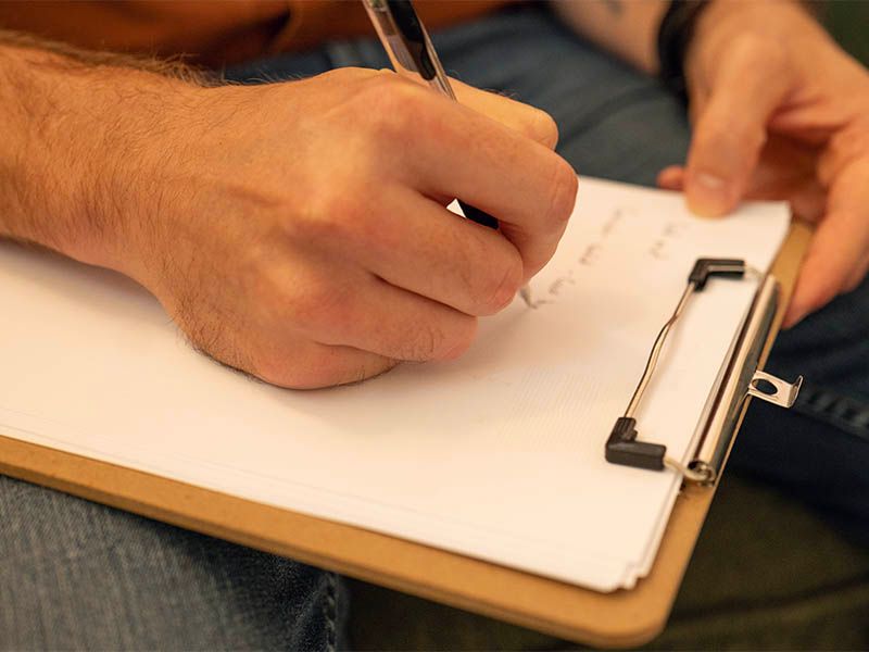 Person writing on a clipboard with a pen, close-up.