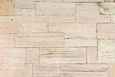 A close-up of a wall made of rectangular, light beige, horizontally stacked stone tiles with a natural, textured finish.