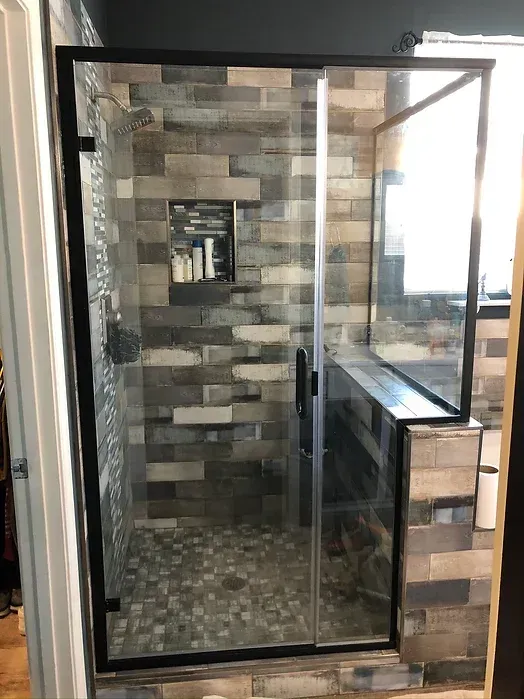 A bathroom with a walk in shower with a glass door and a brick wall.