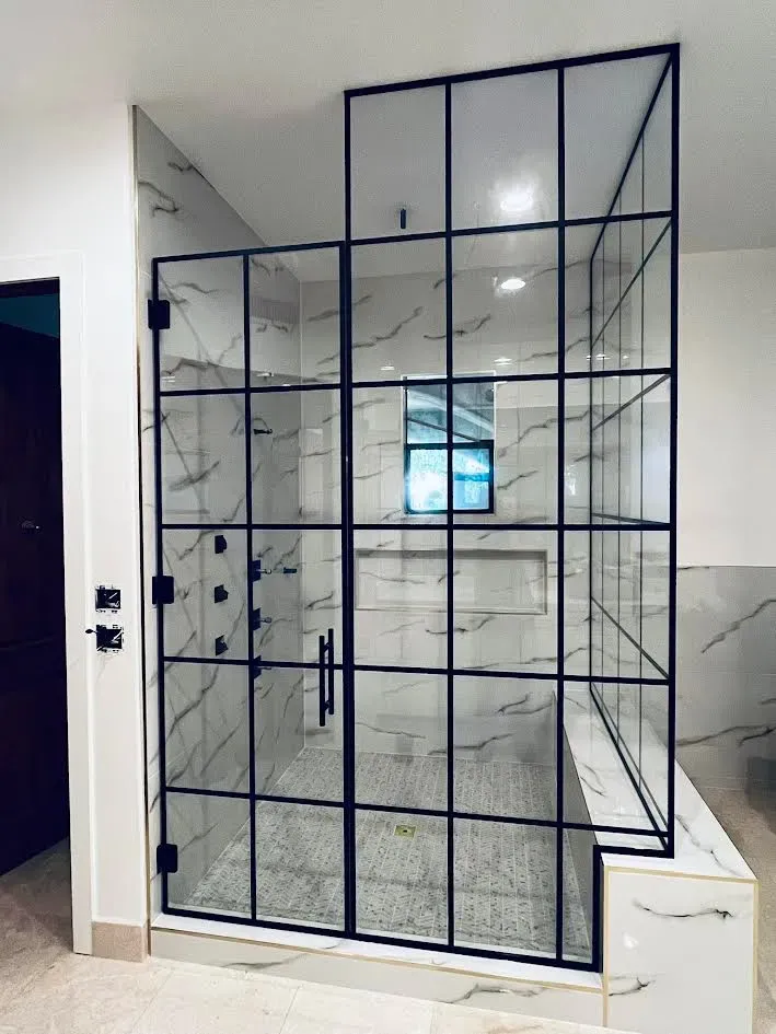 A bathroom with a walk in shower with a black frame.