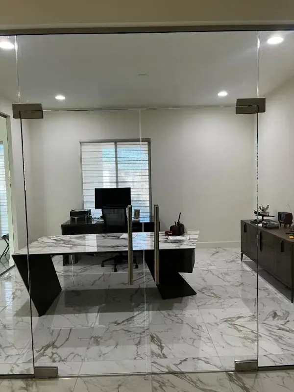 A room with a desk and chairs and a glass door.