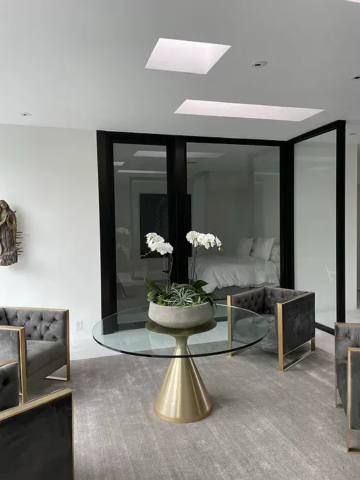 A living room with a glass table and chairs and a vase of flowers on it.