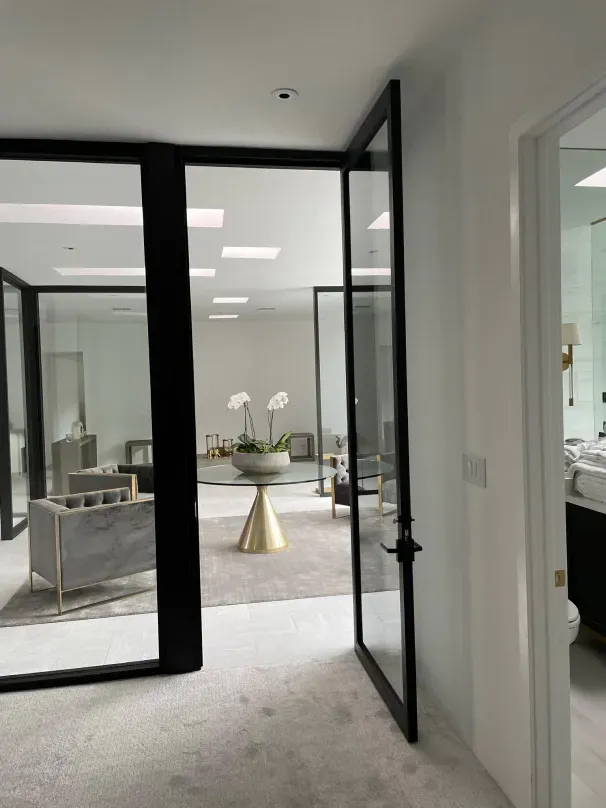 A hallway with a glass door leading to a living room and a bathroom.