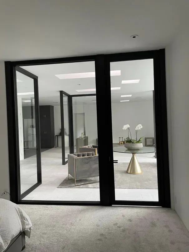 A bedroom with a large glass door leading to a living room.
