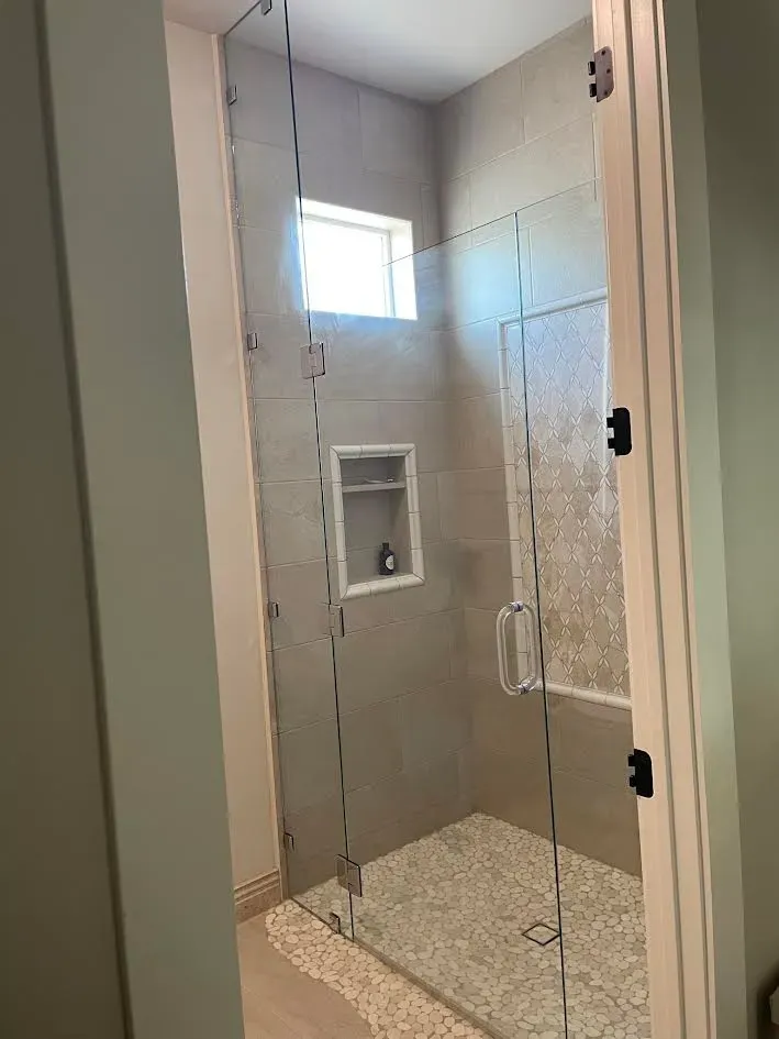 A bathroom with a glass shower door and a window.