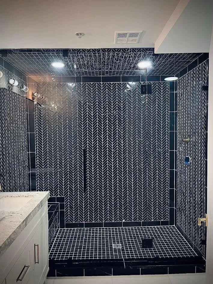 A bathroom with a walk in shower and black and white tiles.