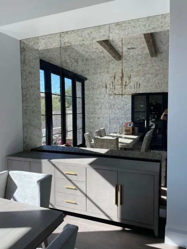 A dining room with a table and chairs and a mirrored wall.