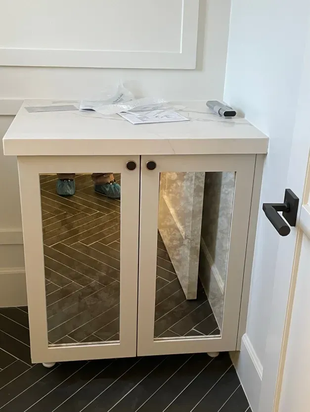 A white cabinet with mirrored doors in a bathroom.