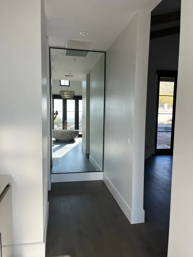 A hallway with a large mirror on the wall leading to a bathroom.