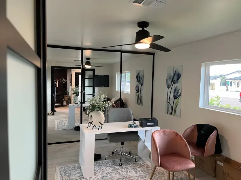 A room with a desk , chairs and a ceiling fan.