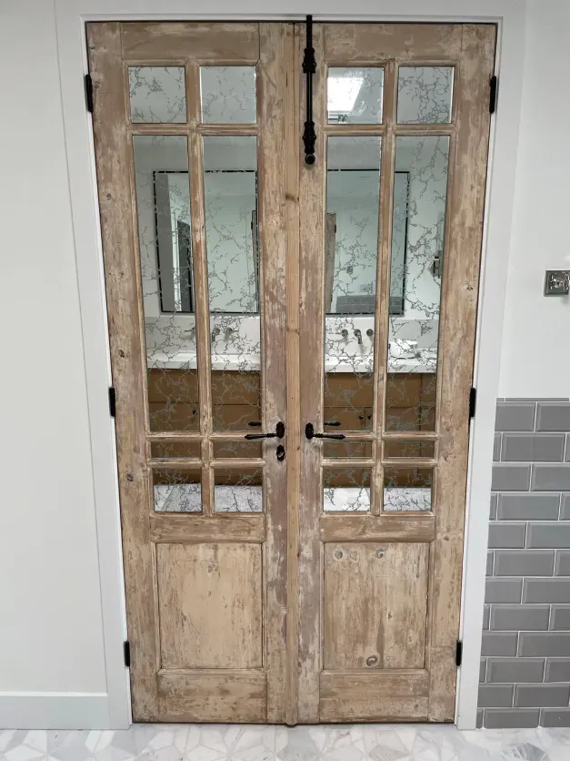 A pair of wooden doors leading to a bathroom with two sinks.