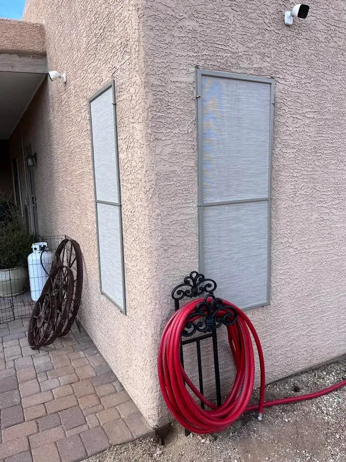 A red hose is sitting on the side of a building next to a window.