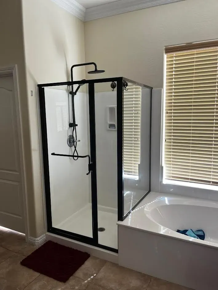A bathroom with a bathtub and a shower with a black frame.