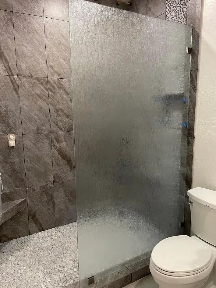 A bathroom with a toilet and a shower stall with a frosted glass door.