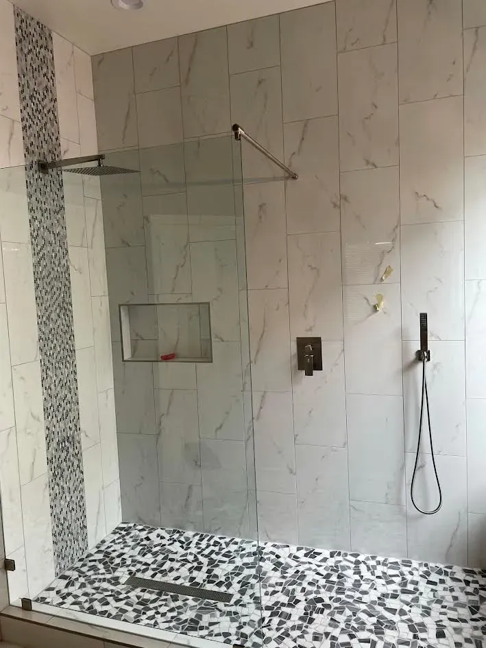 A walk in shower with a glass door and a tiled floor.