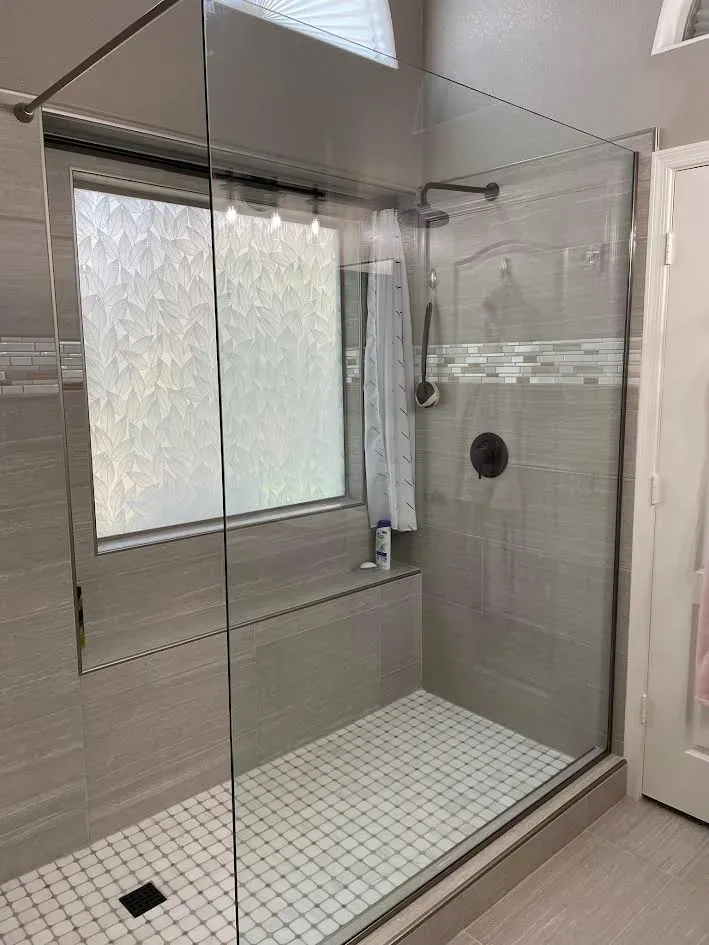 A bathroom with a walk in shower with a glass door and a window.