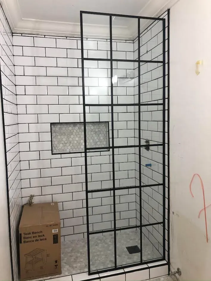 A bathroom with white tiles and a black shower door.