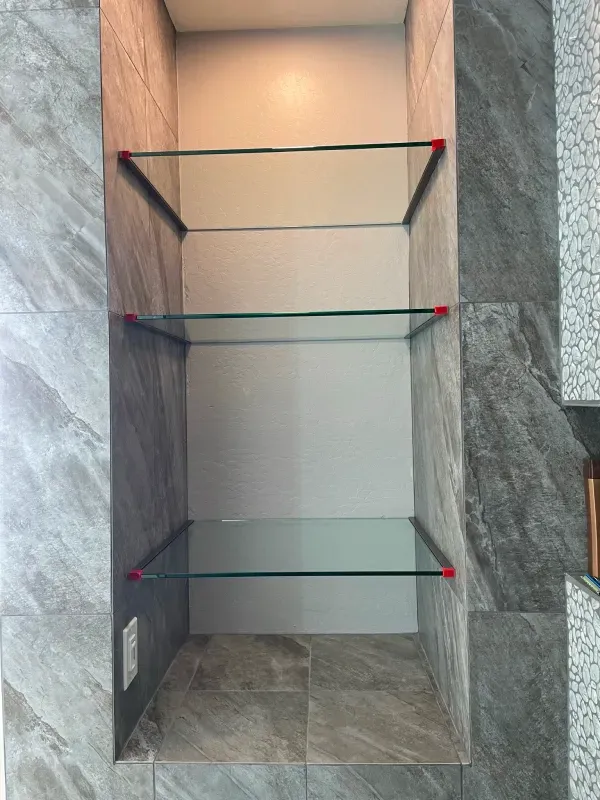 A narrow shelf with three glass shelves in a corner of a room.