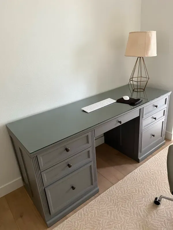 A gray desk with drawers and a lamp in a room.