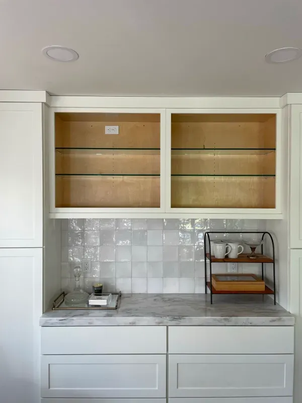 A kitchen with white cabinets , marble counter tops , and glass shelves.