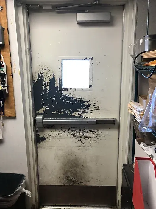 A dirty door with a small window in the middle of it.