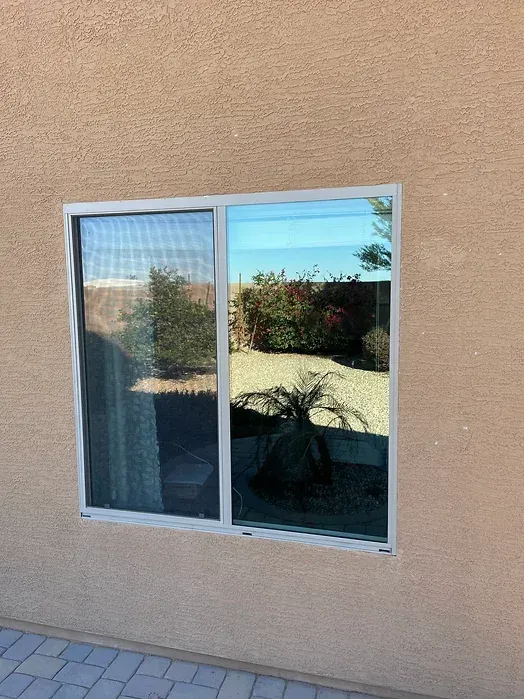 A window on the side of a building with a reflection of trees in it.