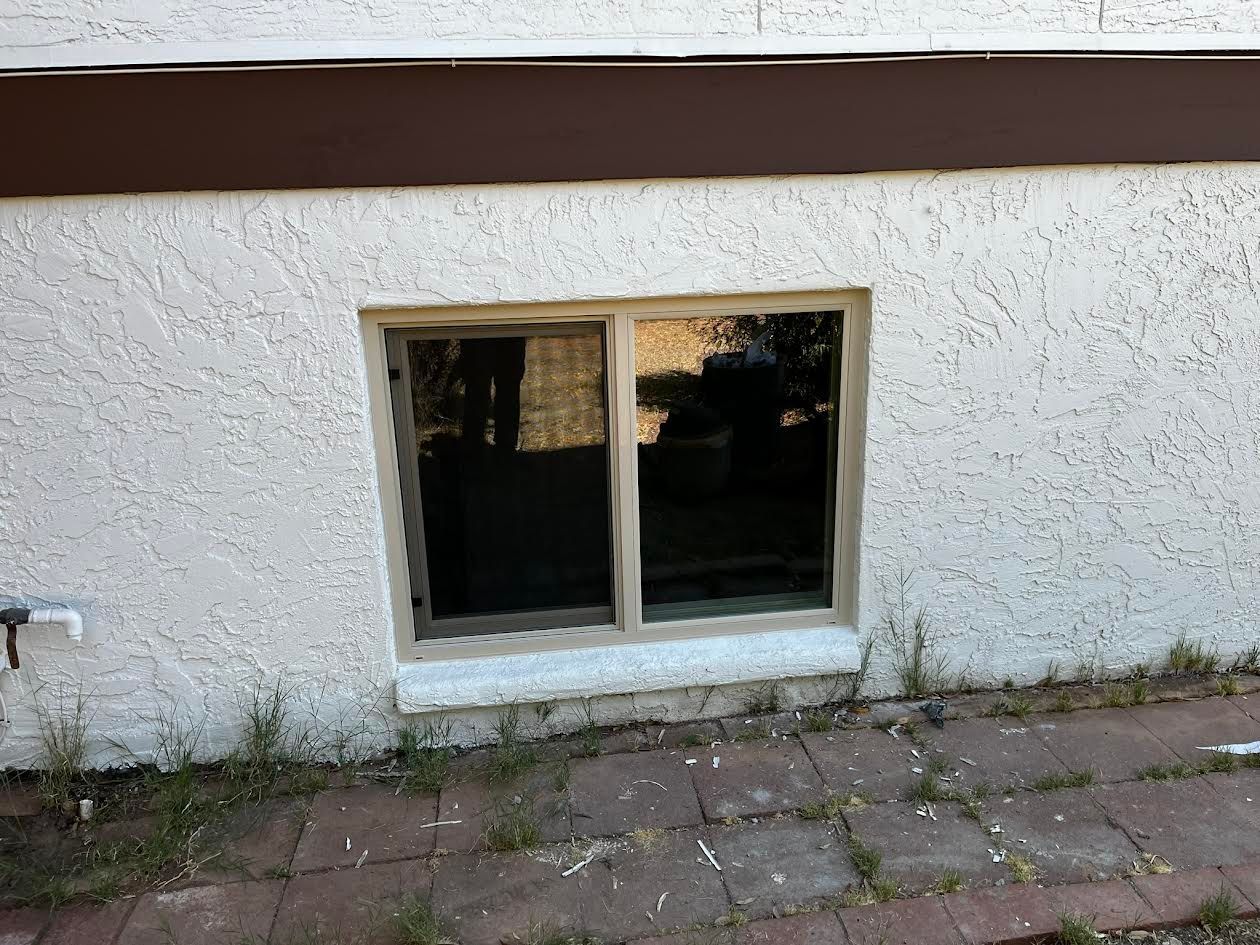 A window on the side of a white building with a brown trim.