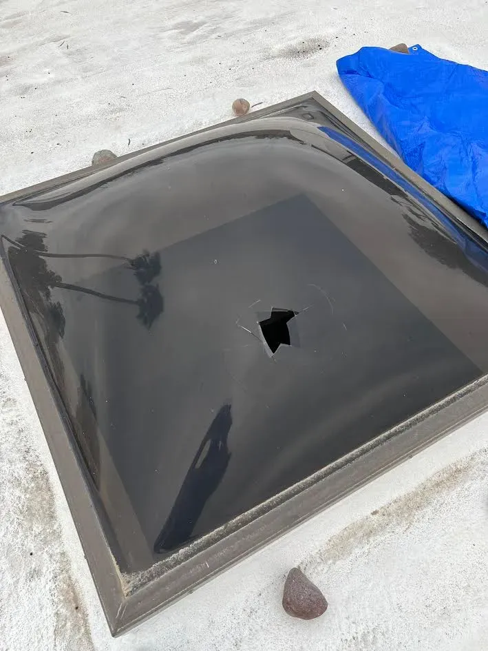 A skylight with a hole in it is sitting on top of a white roof.