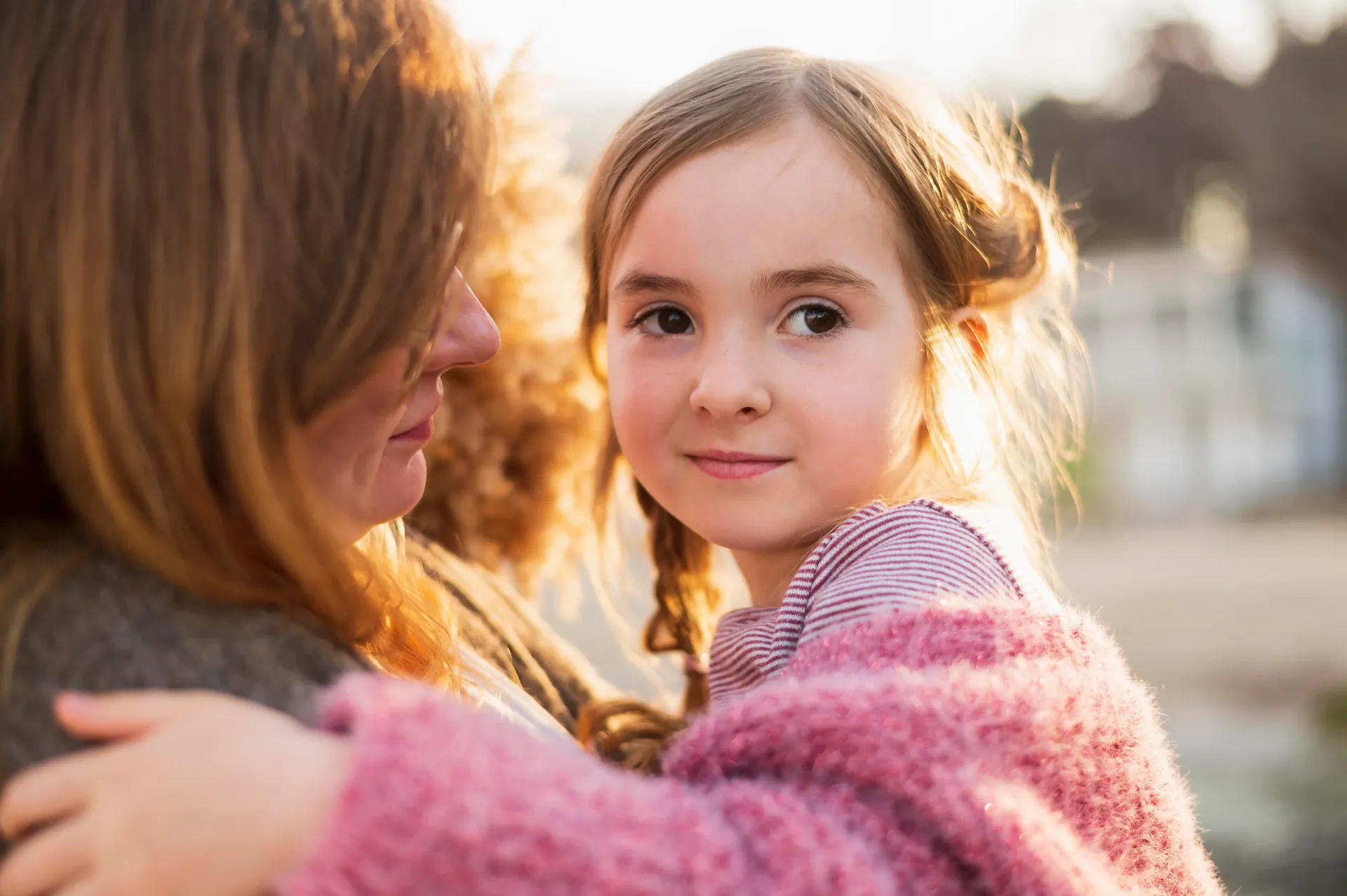 A person holds a child close, both bathed in the warm, golden light of sunset.