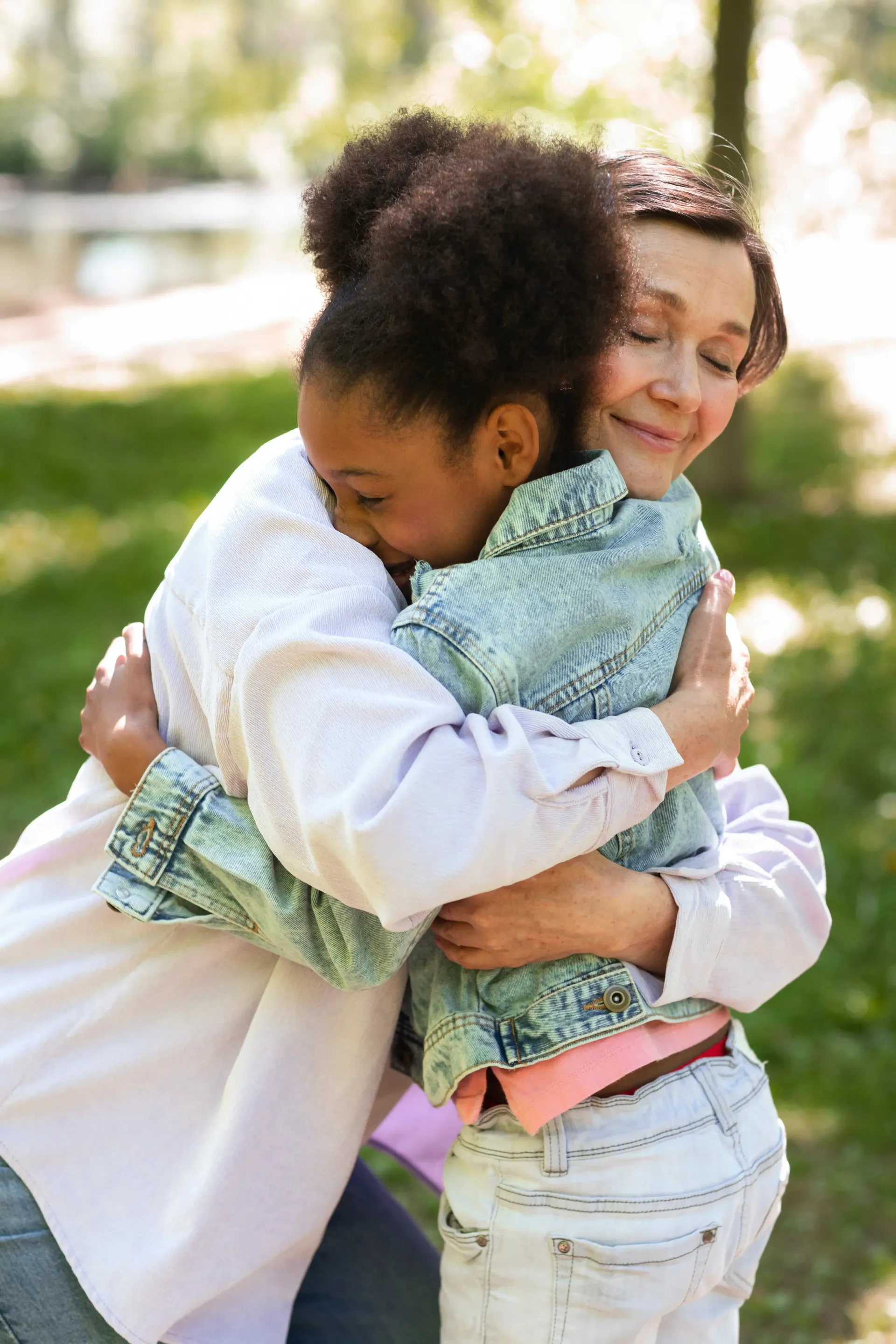 Two people embracing warmly in a park, with soft smiles on their faces.
