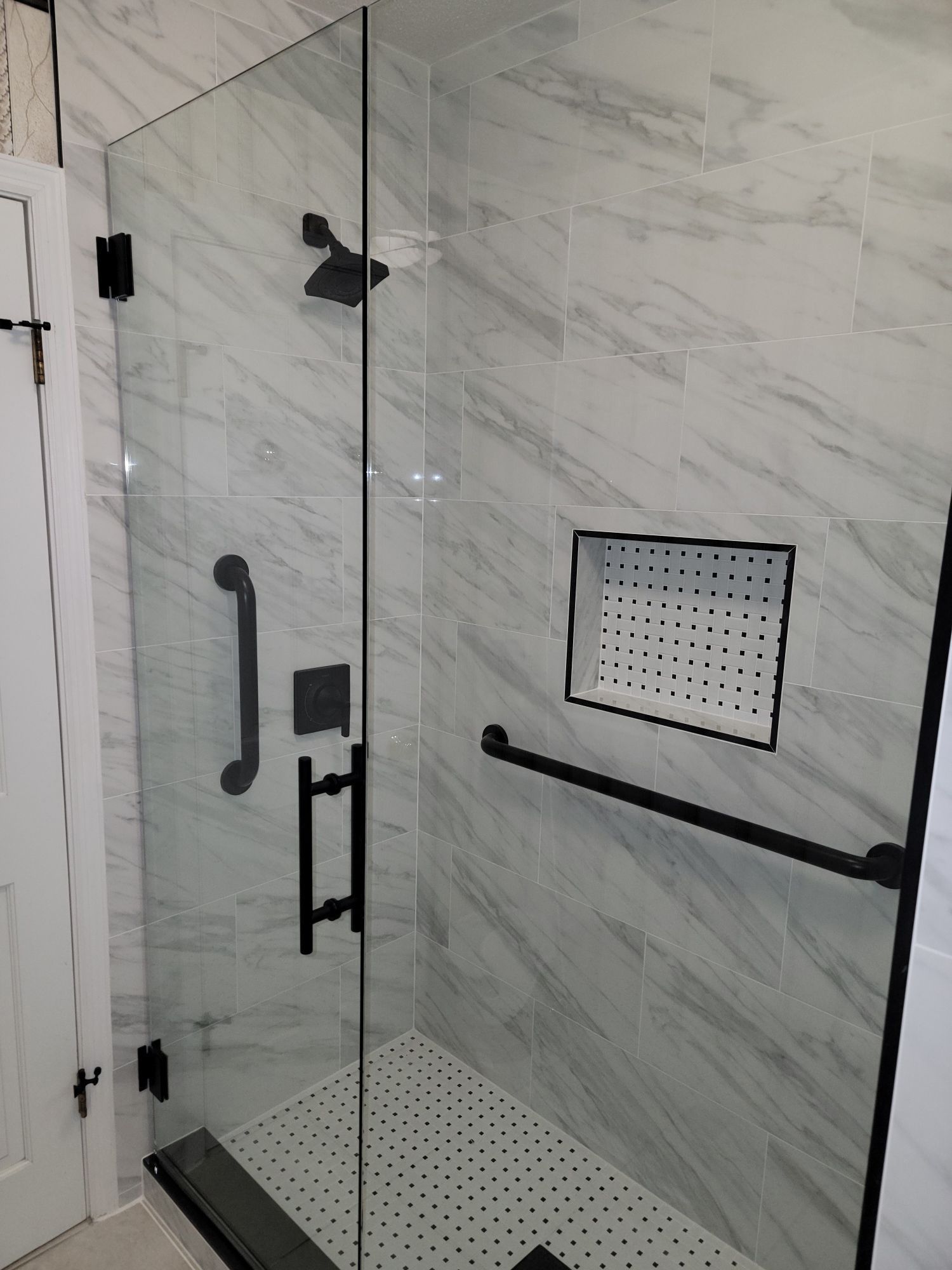 Accessible walk-in shower with glass door, marble tile walls, grab bars, and fold-down seat.