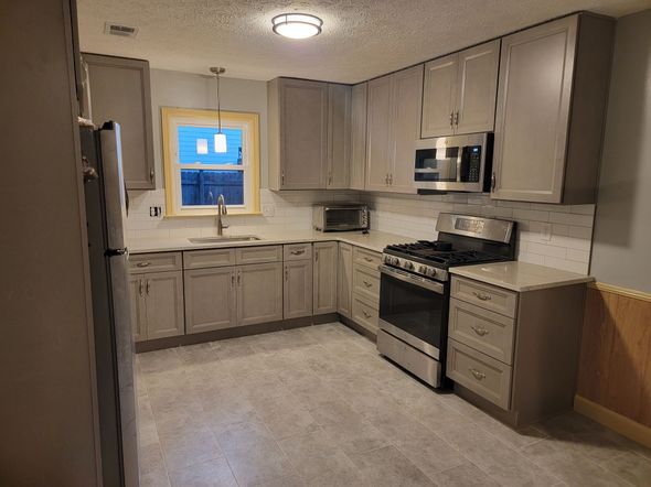 Compact modern kitchen with gray cabinets, stainless steel appliances, and a window over the sink.