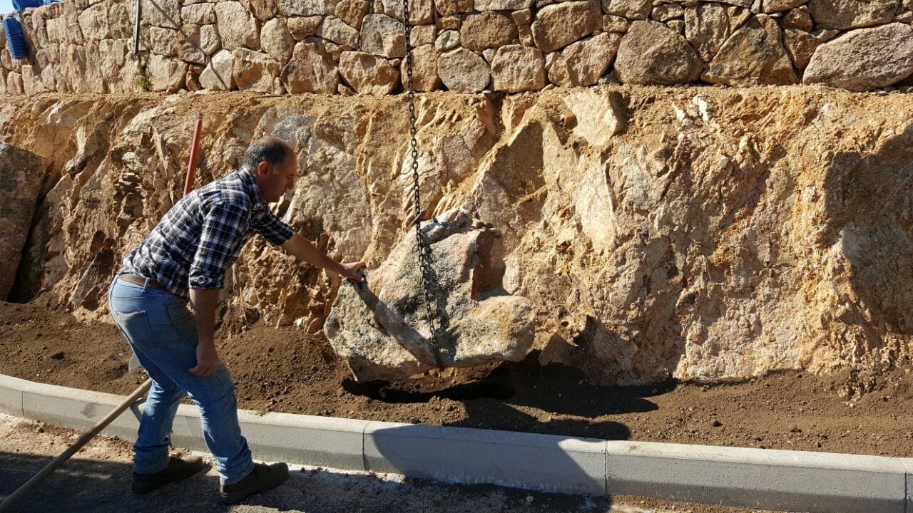 Un uomo spala la terra davanti a un muro di pietra.