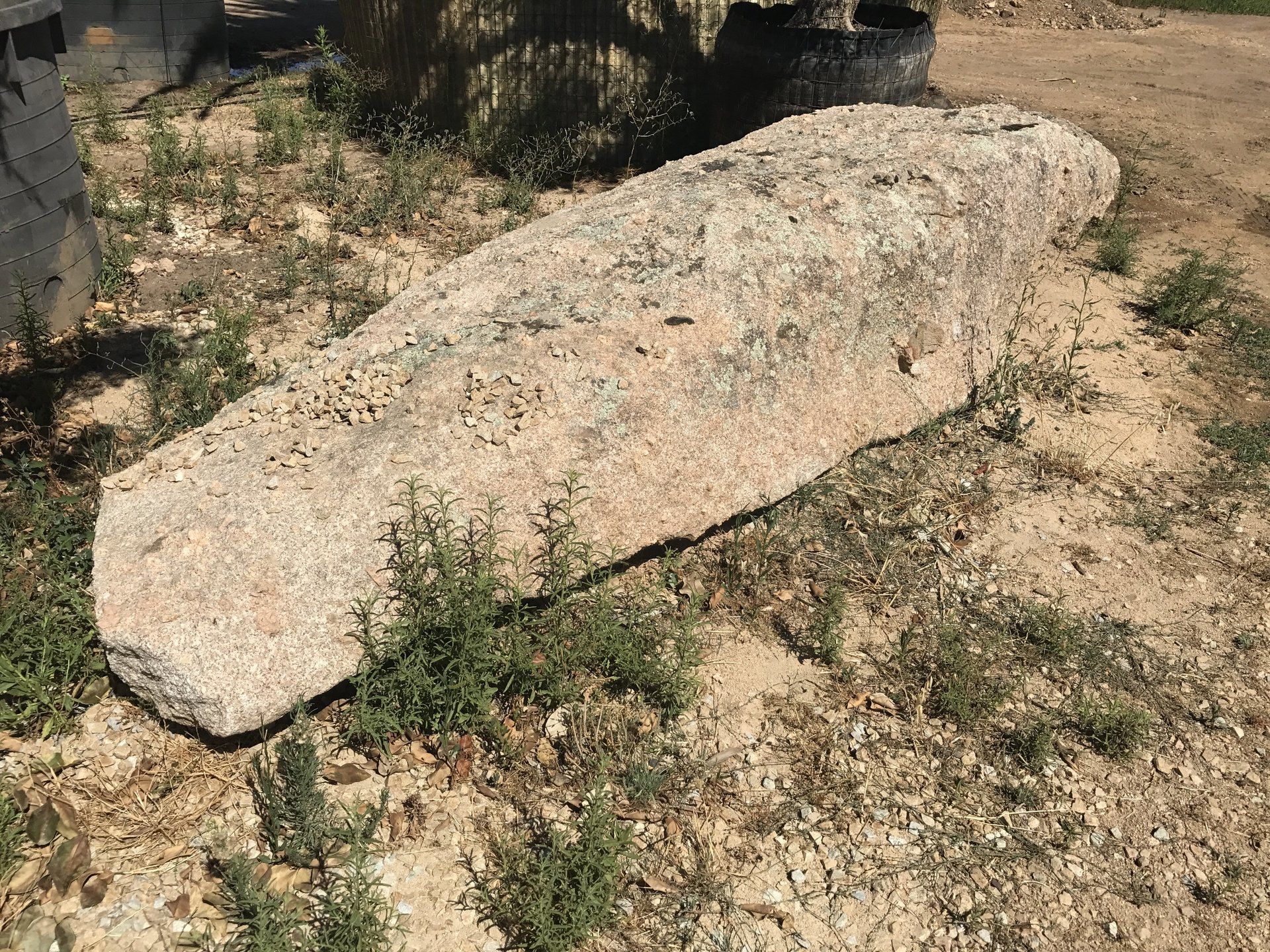 Una grande roccia si trova in cima a un campo sterrato.