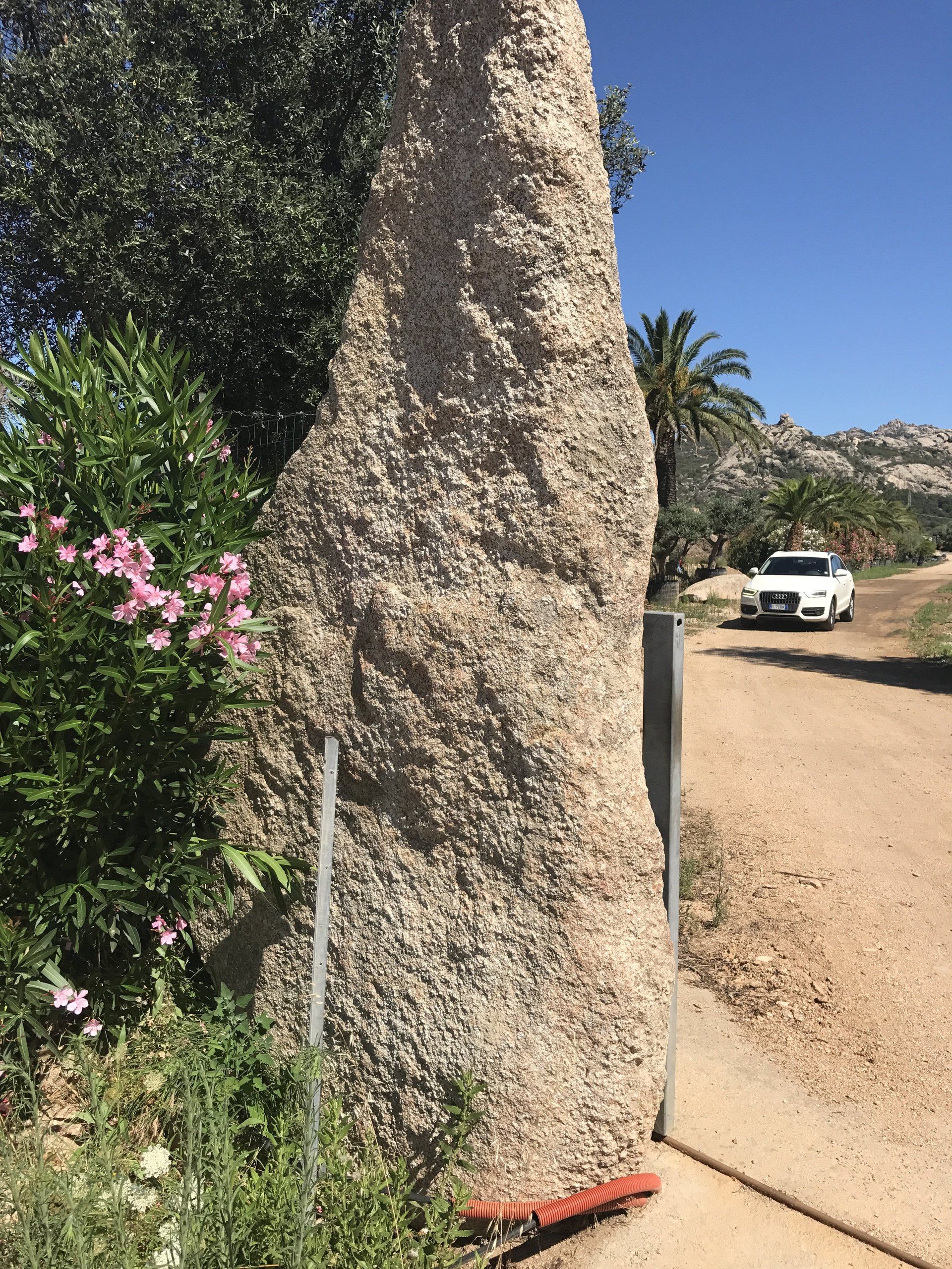 Un'auto bianca è parcheggiata sul lato di una strada sterrata accanto a una grande roccia.