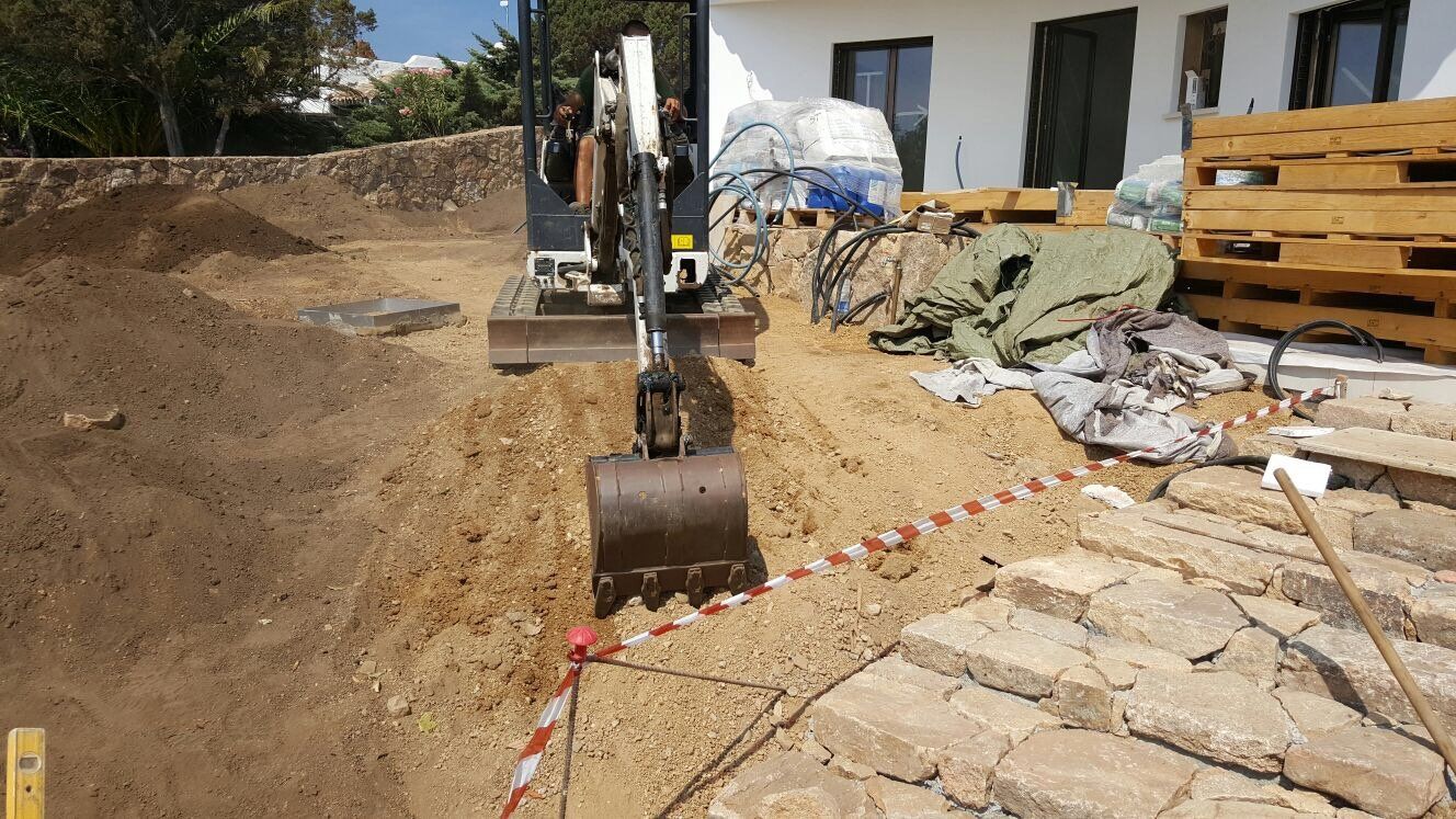 Un escavatore sta scavando una buca nel terreno davanti a una casa.