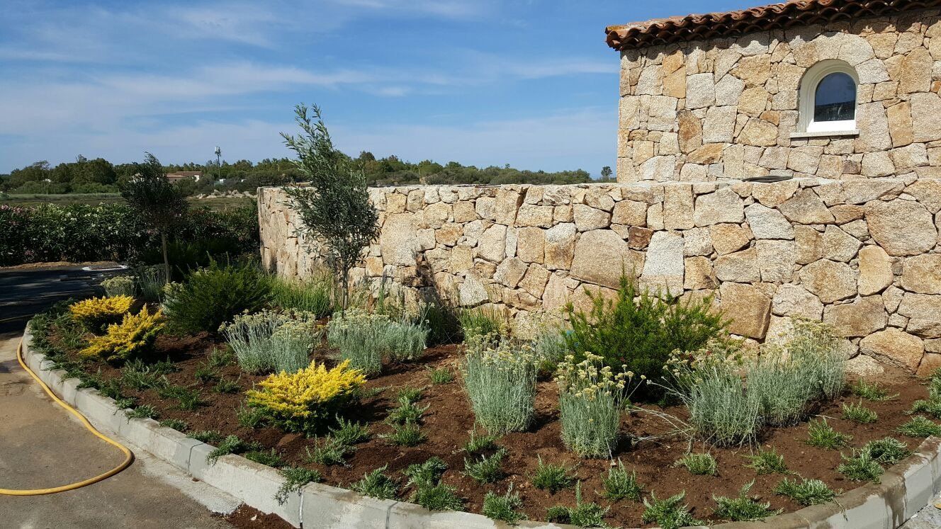 Un muro di pietra con una finestra e un giardino davanti
