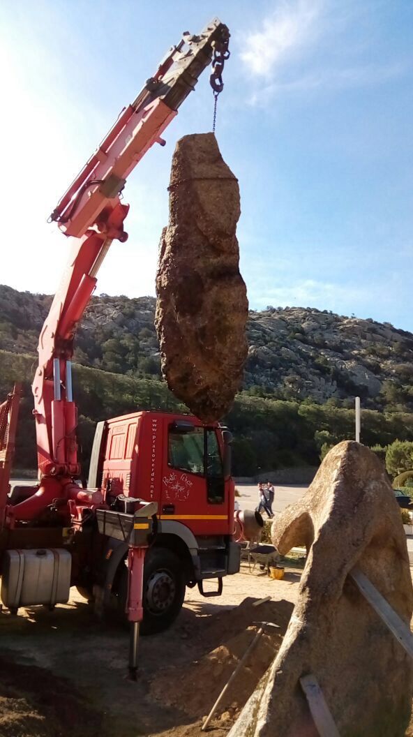 A red truck with an attached crane is lifting a large rock.