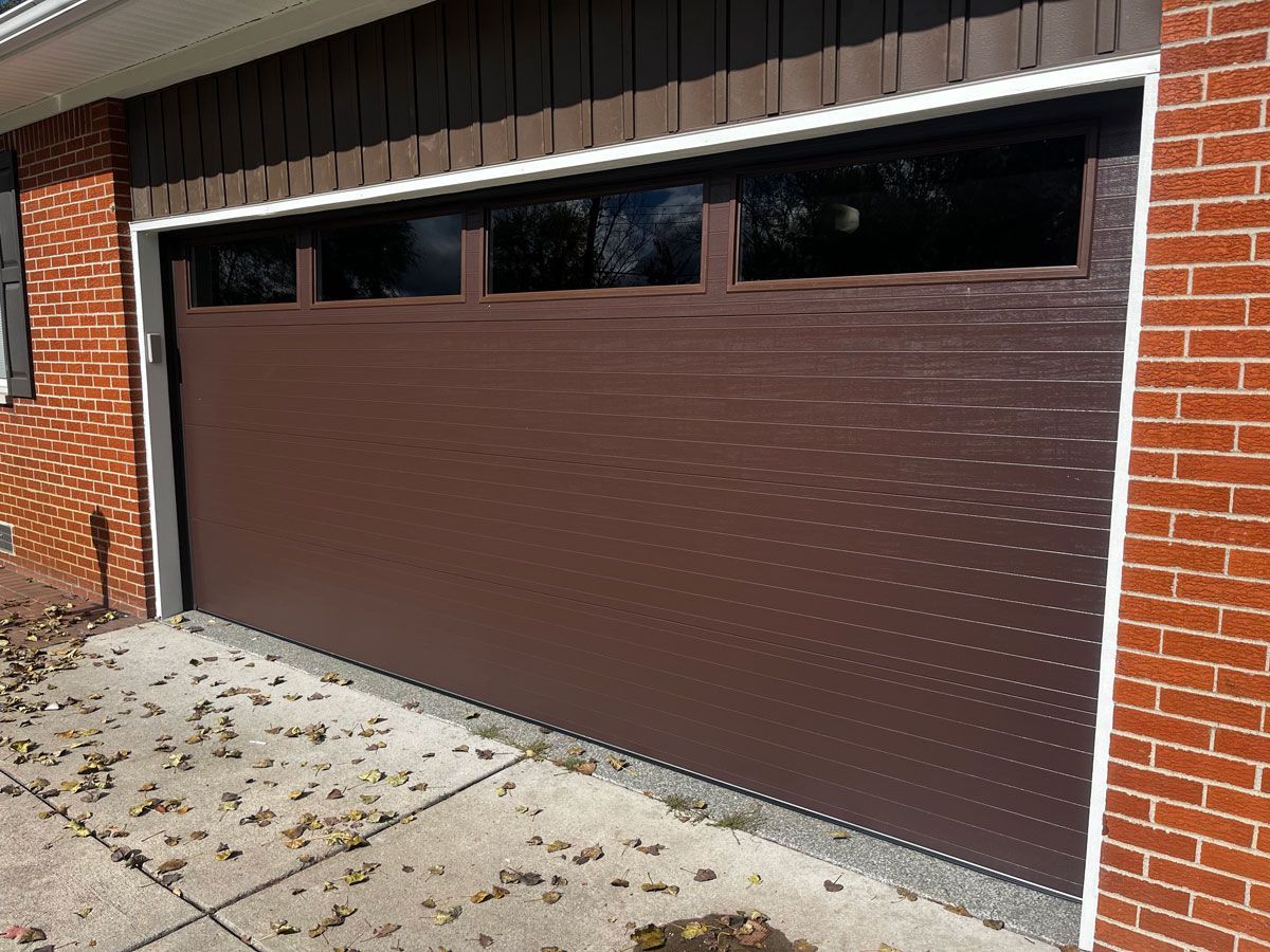 A brown garage door is sitting on the side of a brick building.