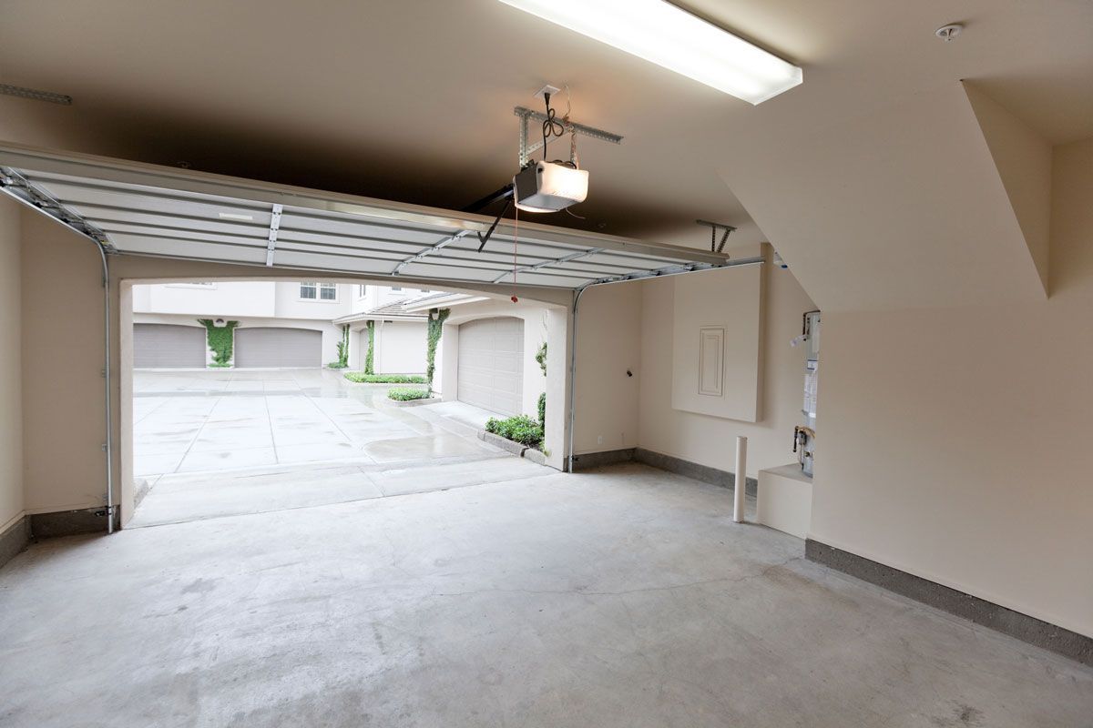 An empty garage with a garage door open and a light on the ceiling.