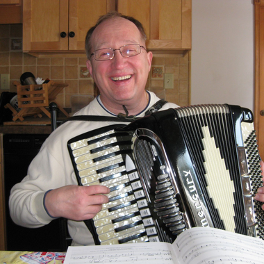 Woman in wheelchair smiles with another woman holding a gift basket and candles in a community hall.