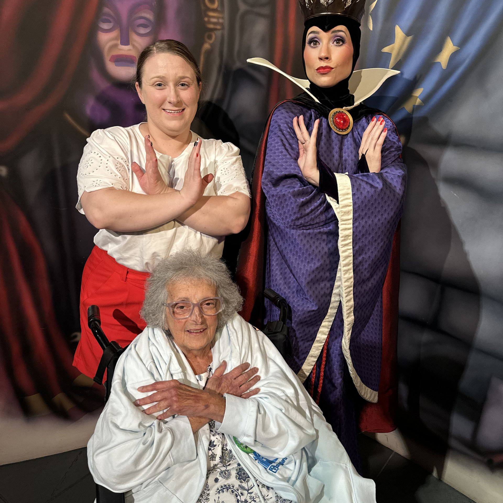 Man, senior woman, and dog in a room. Man hugs dog and looks at woman. Woman in floral top looks at man, mouth open.