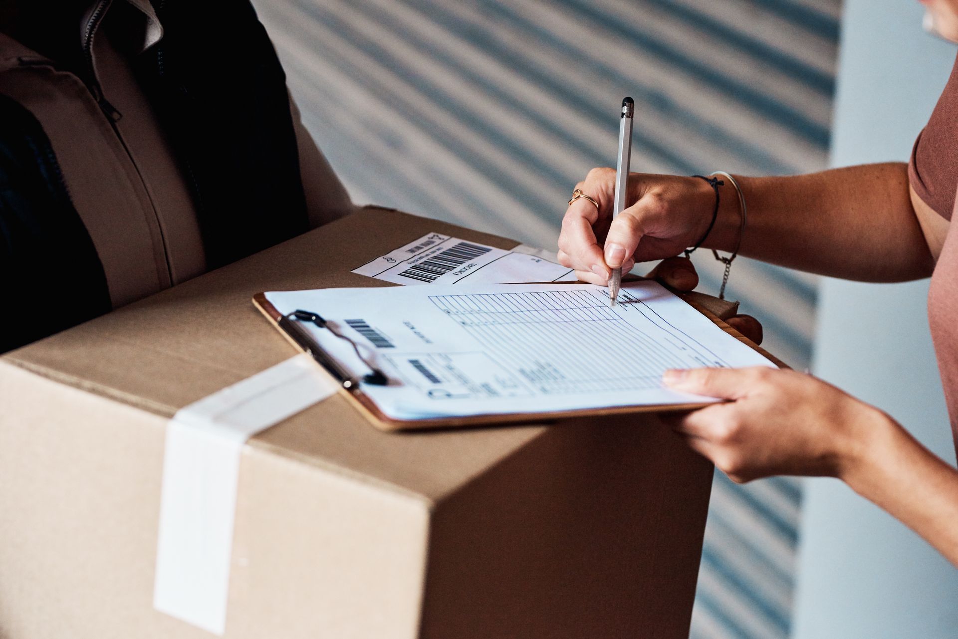 Person signing a delivery form on a cardboard box at a doorstep