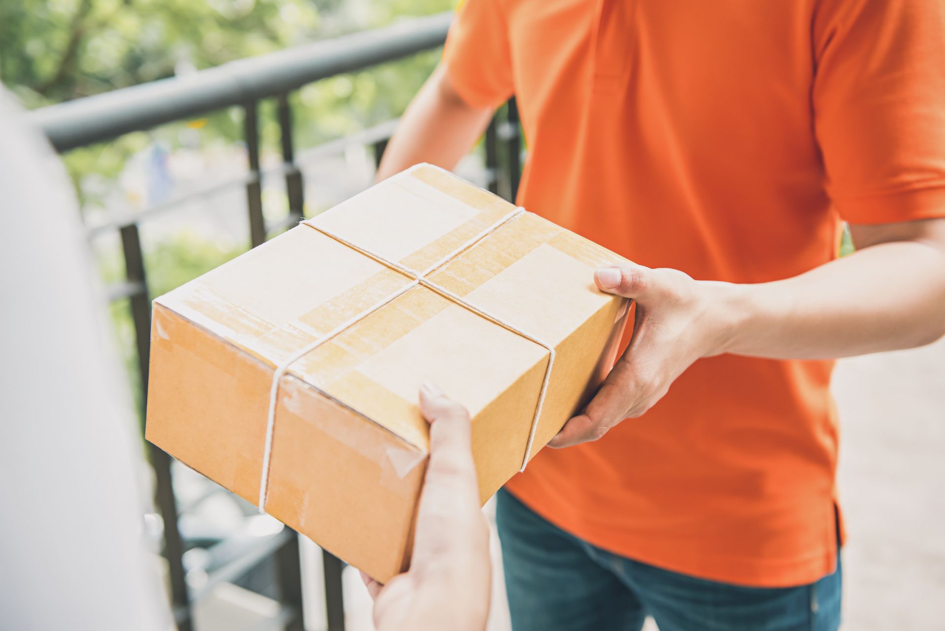 Person in an orange shirt handing over a taped cardboard box outdoors
