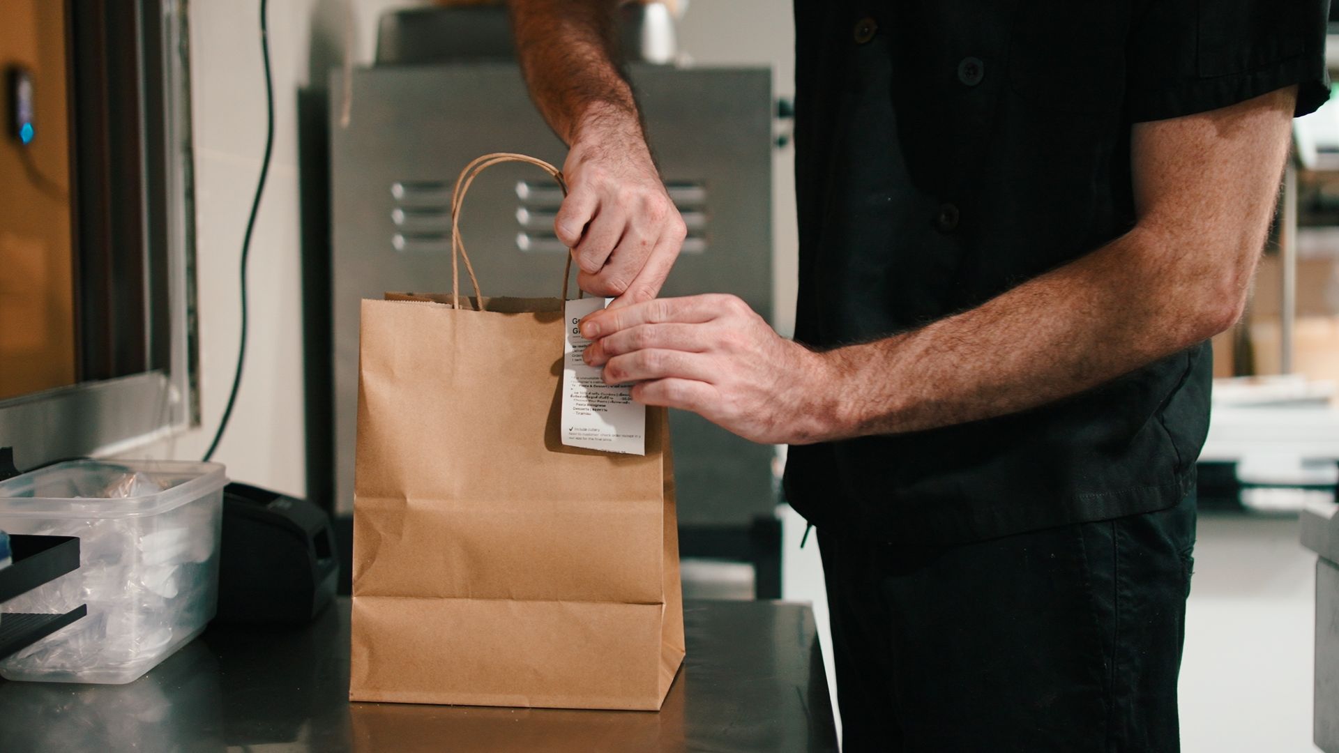 Person sealing a brown paper bag with a sticker on a kitchen counter
