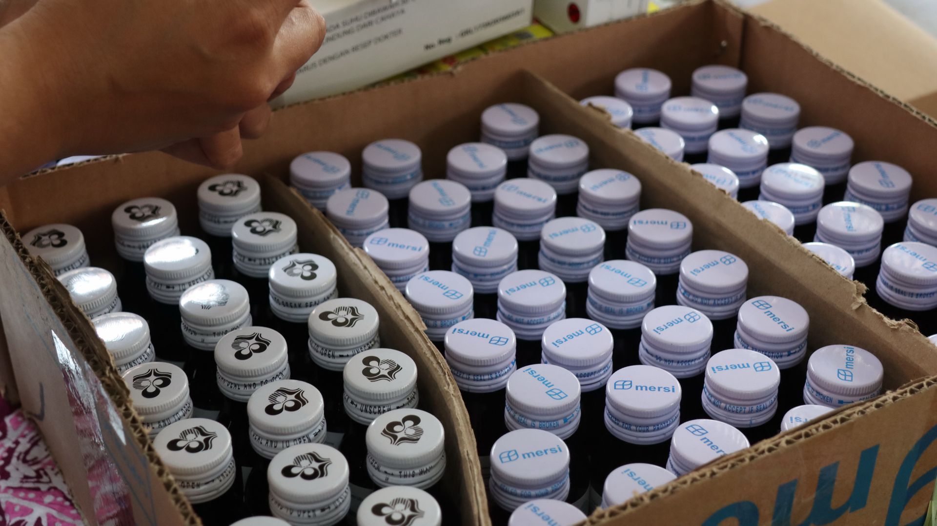 Cardboard box filled with rows of small white-capped bottles with printed labels