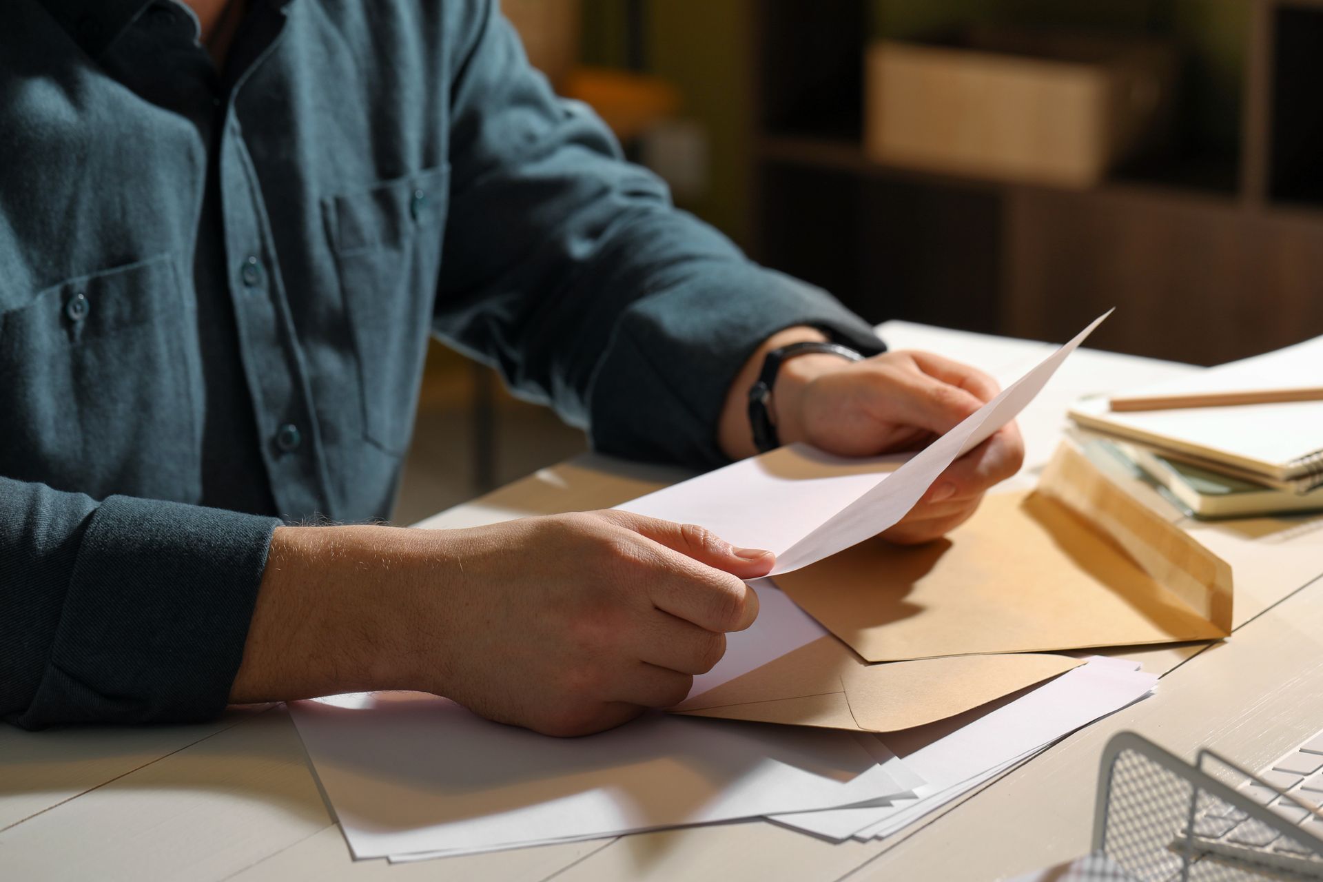 Person in a blue shirt sorting papers at a desk with envelopes and documents