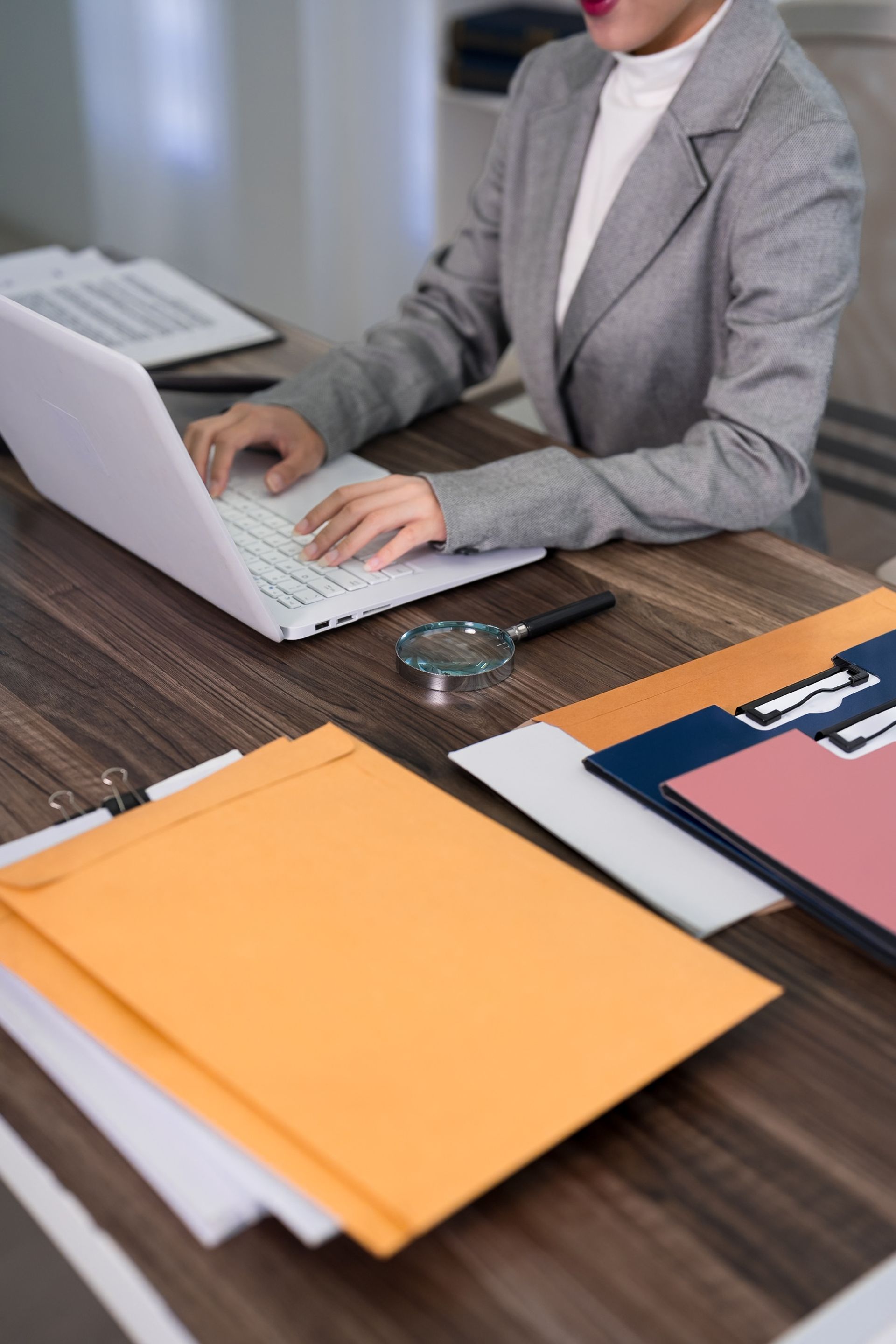 Person typing on a laptop at a desk with folders and office supplies