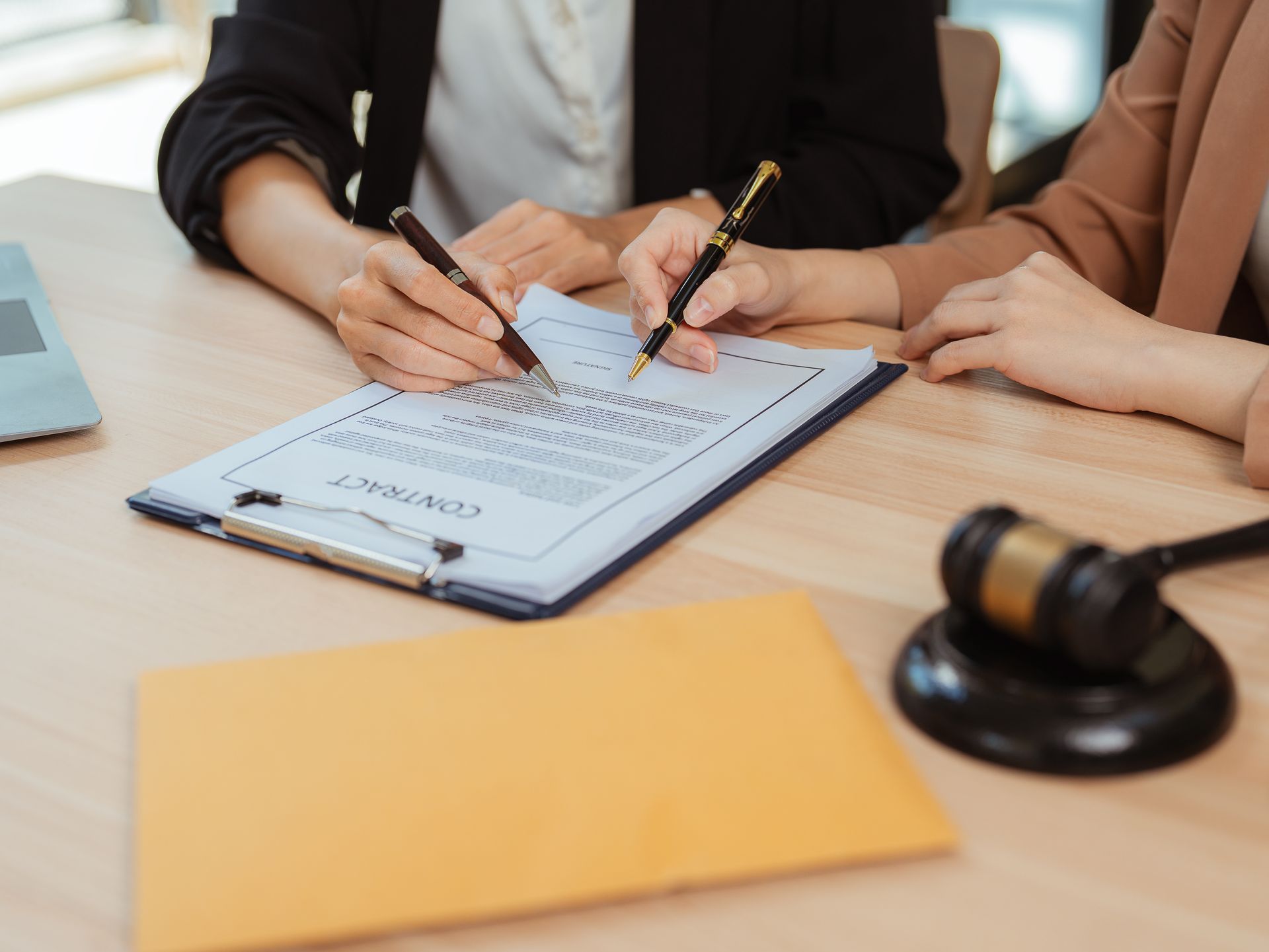 People signing legal documents at a desk with a gavel and yellow folder